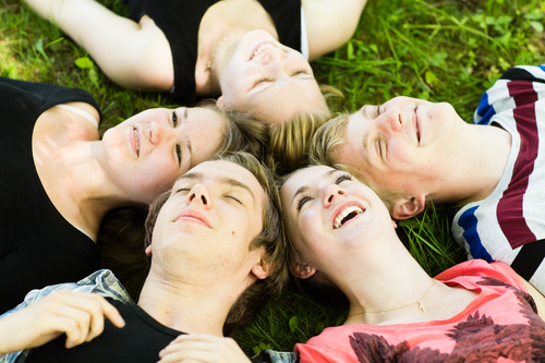 Unga människor som ligger på en gräsmatta och ser glada ut.